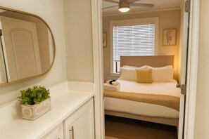 A hotel room with a bed, a bedside table with a plant, a window with blinds, and a ceiling fan. - Portage Park 1BR Retreat (Chicago)