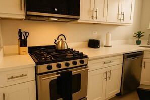 A kitchen with white cabinets, a stainless steel stove, a toaster, and a dishwasher. - Portage Park 1BR Retreat (Chicago)