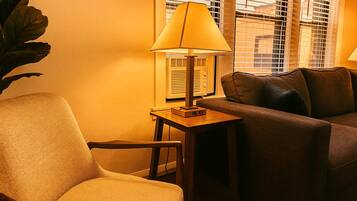 A cozy living room with a sofa, a chair, a table with a lamp, and a large plant.
