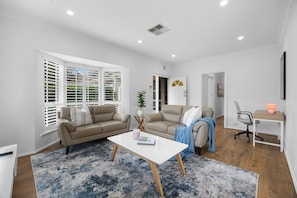 A modern living room with two sofas, a coffee table, and a desk with a chair. - Burleigh: Easy Coastal Living on Broadway (Glenelg South)