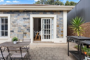 A house with a stone exterior, a patio with a table and chairs, and a barbecue grill. - Burleigh: Easy Coastal Living on Broadway (Glenelg South)