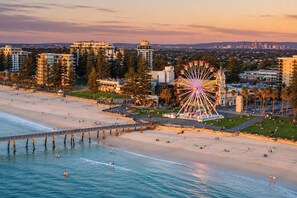 A beachside view with a Ferris wheel, beachfront promenade, and high-rise buildings in the background. - Burleigh: Easy Coastal Living on Broadway (Glenelg South)