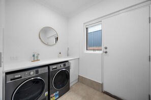 A laundry room with two front-loading washers, a sink, a mirror, and a door with a window. - Burleigh: Easy Coastal Living on Broadway (Glenelg South)