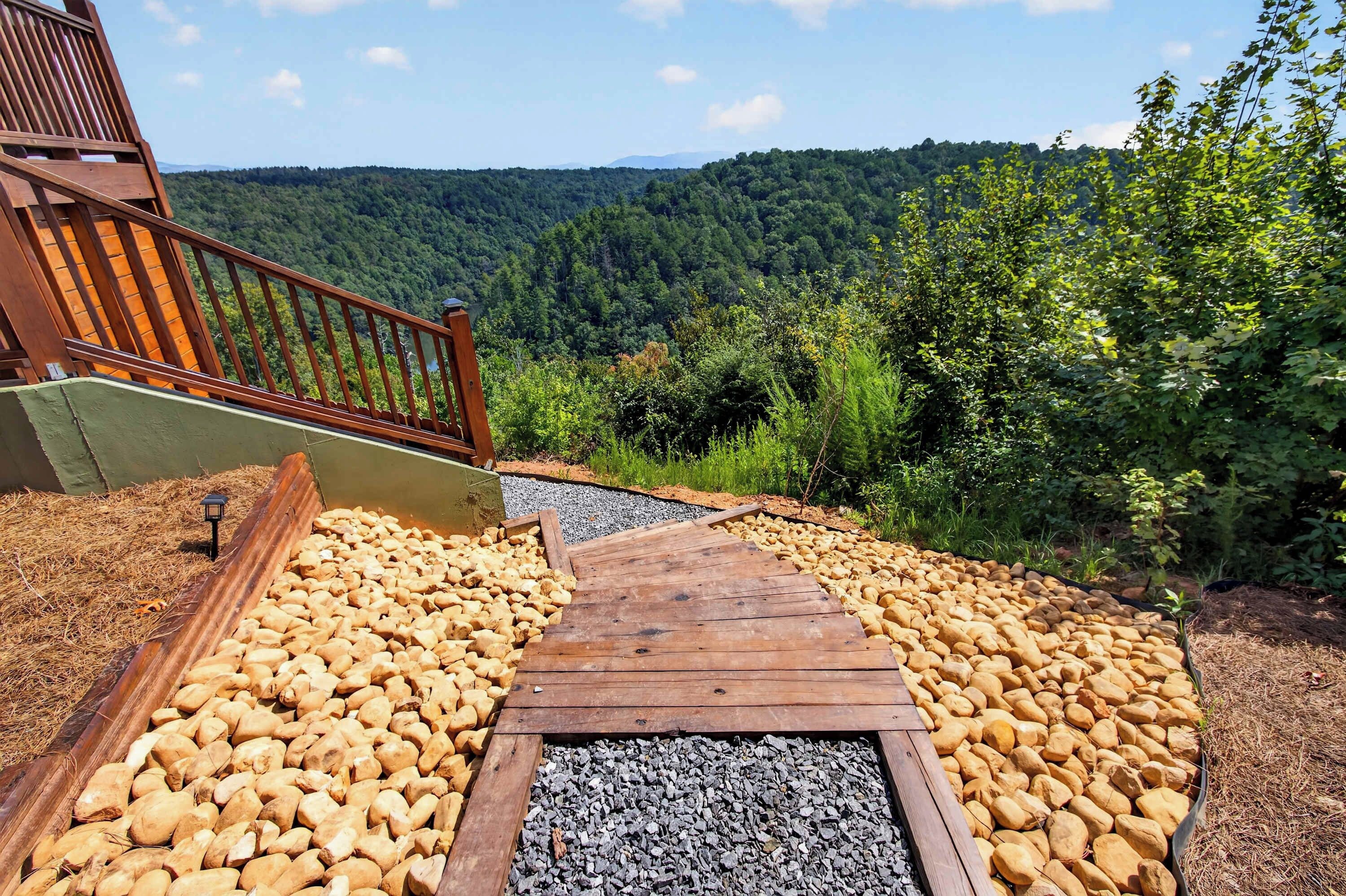 A wooden pathway leading to a deck with a view of a forested hillside.