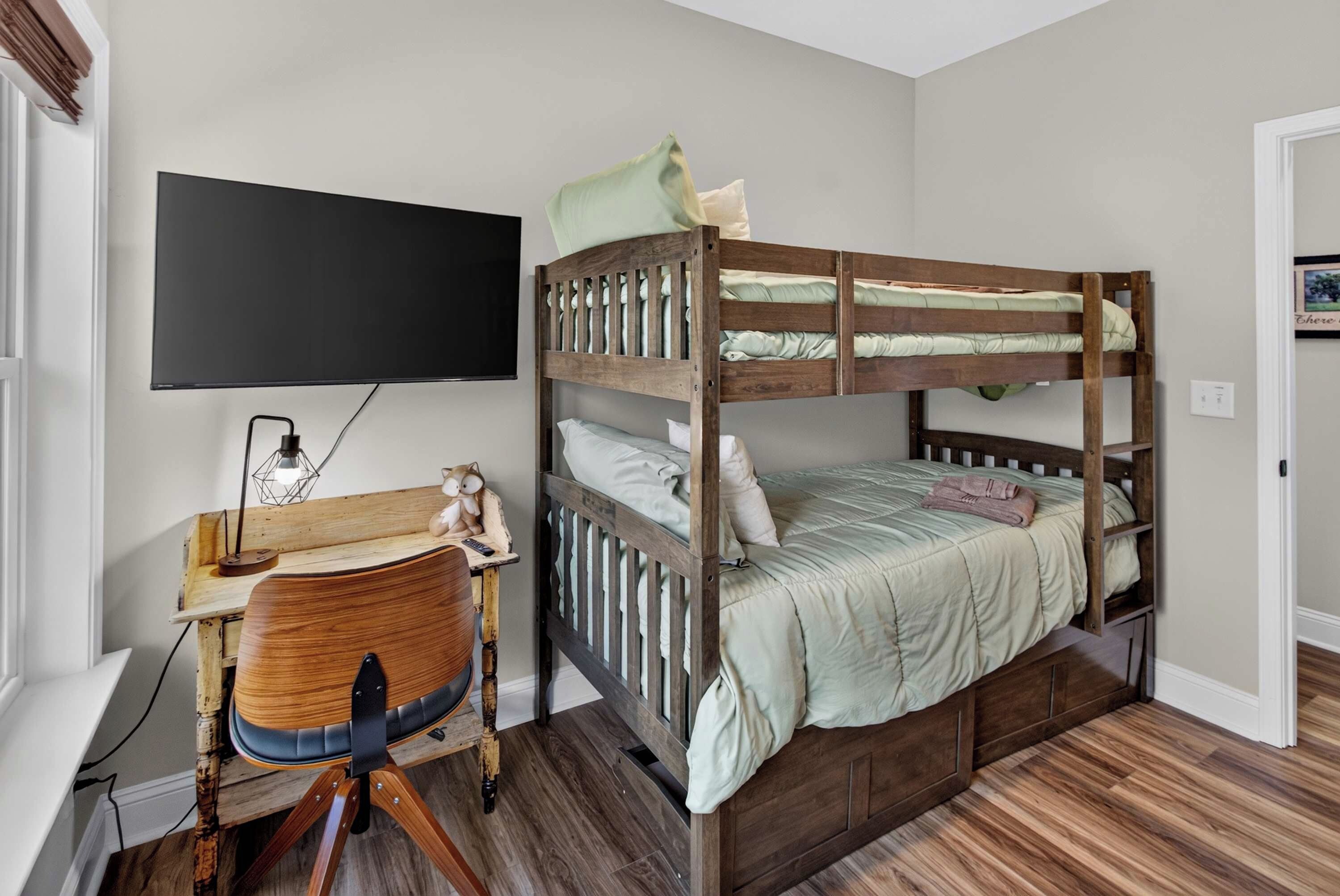 A bunk bed with a desk and chair, a flat-screen TV, and a wooden floor.