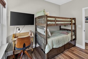 Un letto a castello con scrivania e sedia, una TV a schermo piatto e un pavimento in legno.