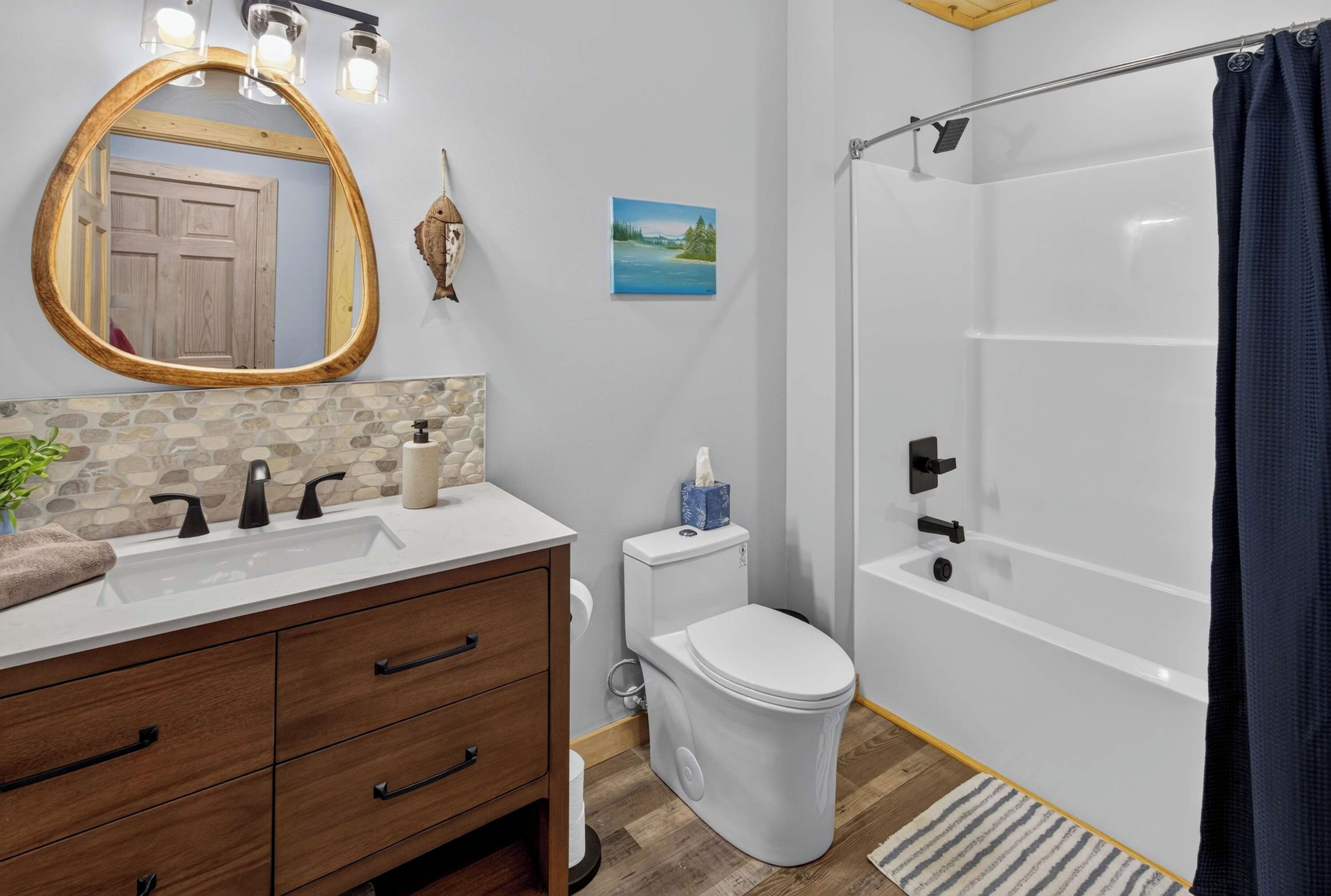 A bathroom with a wooden vanity, a white toilet, a shower with a glass door, and a painting on the wall.