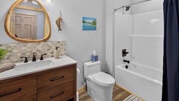 A bathroom with a wooden vanity, a white toilet, a shower with a glass door, and a painting on the wall.