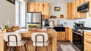 Eine moderne Küche mit Holzschränken, einem Edelstahlkühlschrank, einem eingebauten Backofen und einem Essbereich mit zwei Stühlen.