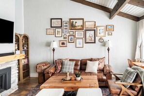 A cozy living room with a brown leather sofa, a wooden coffee table, and a fireplace. - Walk to Greek Peak Lifts - Mtn View & Balcony (Cortland)