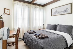 A bedroom with a bed, a desk, a chair, a fan, and a painting on the wall. - Walk to Greek Peak Lifts - Mtn View & Balcony (Cortland)