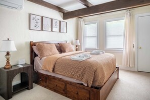 A bedroom with a wooden bed, a nightstand with a lamp, a dresser, and a window with curtains. - Walk to Greek Peak Lifts - Mtn View & Balcony (Cortland)
