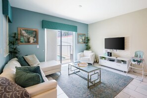 Ein Wohnzimmer mit Sofa, Couchtisch, Fernseher und Blick ins Freie.