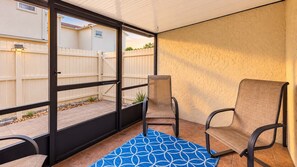 Ein überdachter Patio-Bereich mit schwarzem Metallgeländer, zwei Stühlen und einer blau gemusterten Teppich.