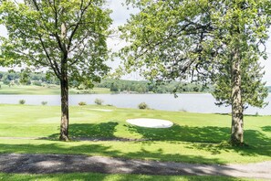 Ein Golfplatz mit einem Wasserhindernis im Hintergrund, Bäumen und blauem Himmel.