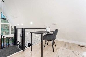 A modern interior with a staircase, a table with a chair, and a view of trees through large windows.