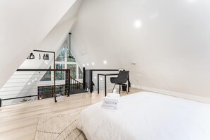 A modern bedroom with a large bed, a staircase, and a view of trees through the windows.