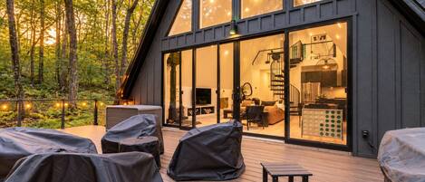 A modern cabin with a large glass door, a deck with covered seating, and a visible kitchen area.