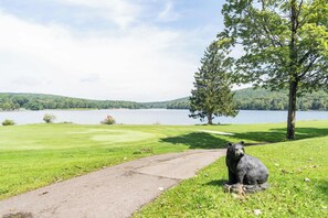 A golf course with a statue of a bear, a lake, and a tree.