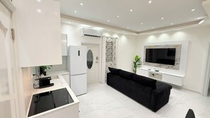 Eine moderne Küche mit Einbauherd, einem weißen Kühlschrank und einem schwarzen Sofa in einem Wohnbereich mit an der Wand befestigtem Flachbildfernseher.