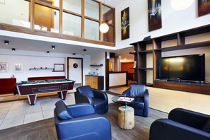 A spacious living area with a pool table, comfortable seating, a large flat-screen TV, and a high ceiling with natural light. - À 300 m des pistes | Piscine couverte sur place (Chantemerle)