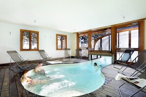 Un bain à remous doté d’une terrasse en bois, entouré de fenêtres aux cadres en bois.