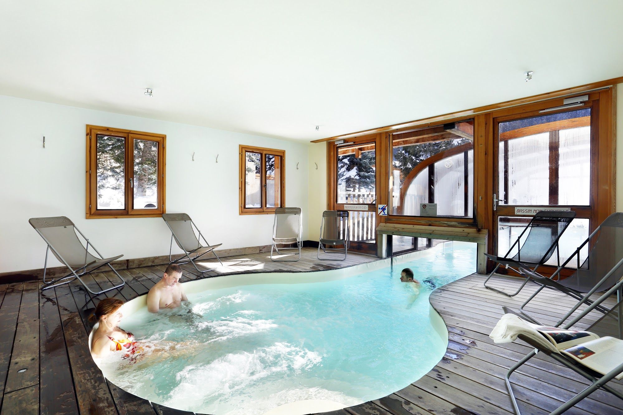 A hot tub with a wooden deck, surrounded by windows with wooden frames.