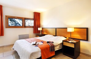 A hotel room with a bed, two bedside tables, a window with curtains, and a radiator. - Proches des pistes | Piscine sur place | Parking (Chantemerle)