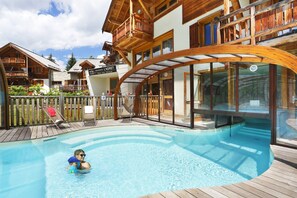 Ein Poolbereich mit Holzterrasse, einem durch Glas geschützten Abschnitt und einem Schild, das ein Wohnhaus und ein Fitnessstudio kennzeichnet.