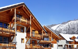 A wooden chalet with multiple balconies, a stone facade, and a view of a snow-covered mountain. - Près des pistes | Piscine chauffée sur place (Chantemerle)