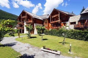Ein Chalet-Hotel mit mehreren Balkonen, einem gepflegten Rasen und einer Bergkulisse.