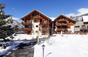 Un chalet en bois doté de plusieurs balcons, entouré de montagnes enneigées.