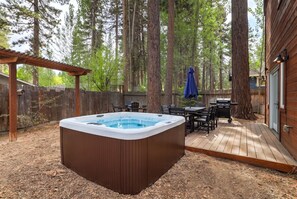 A hot tub in a backyard with a wooden deck, surrounded by tall trees. - Big Pine House! Hot Tub + Dog Friendly + Fire Pit (South Lake Tahoe)