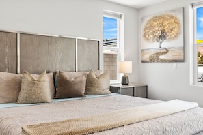 Quarto com uma cama grande, cabeceira, mesa de cabeceira com abajur e um quadro de uma árvore.