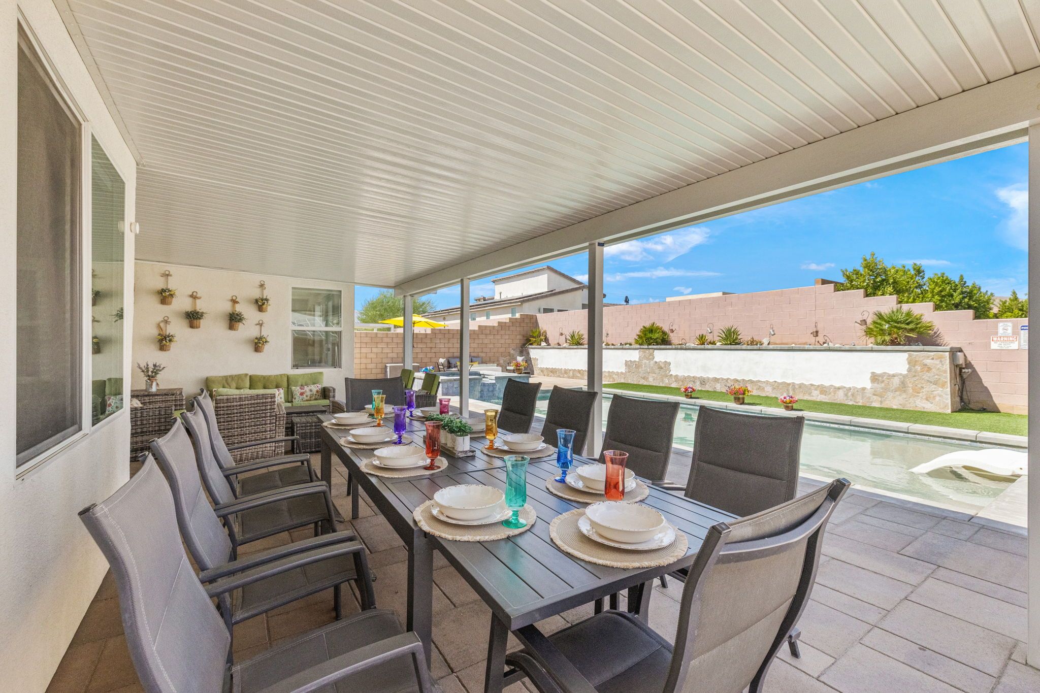 Un patio exterior con mesa lista para comer, rodeado de sillas y vistas a una piscina.