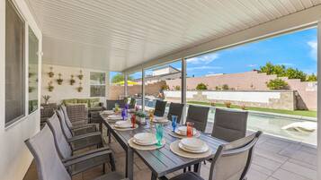 Un patio exterior con mesa lista para comer, rodeado de sillas y vistas a una piscina.