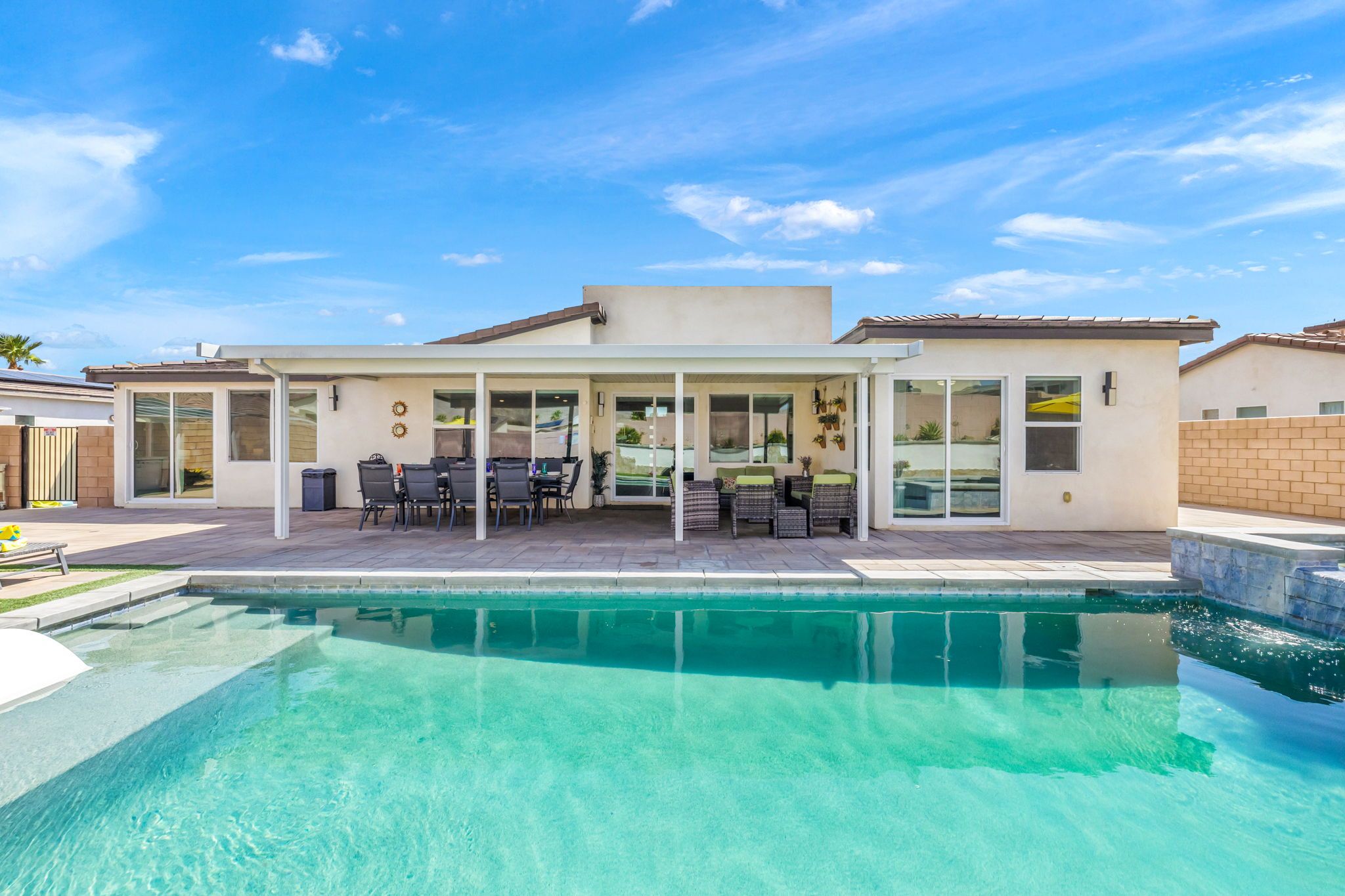 Una casa moderna con piscina, muebles de patio y un espacio exterior cubierto.