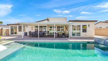 Una casa moderna con piscina, muebles de patio y un espacio exterior cubierto.