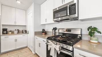 A modern kitchen with white cabinets, stainless steel appliances, a gas stove, and a microwave.