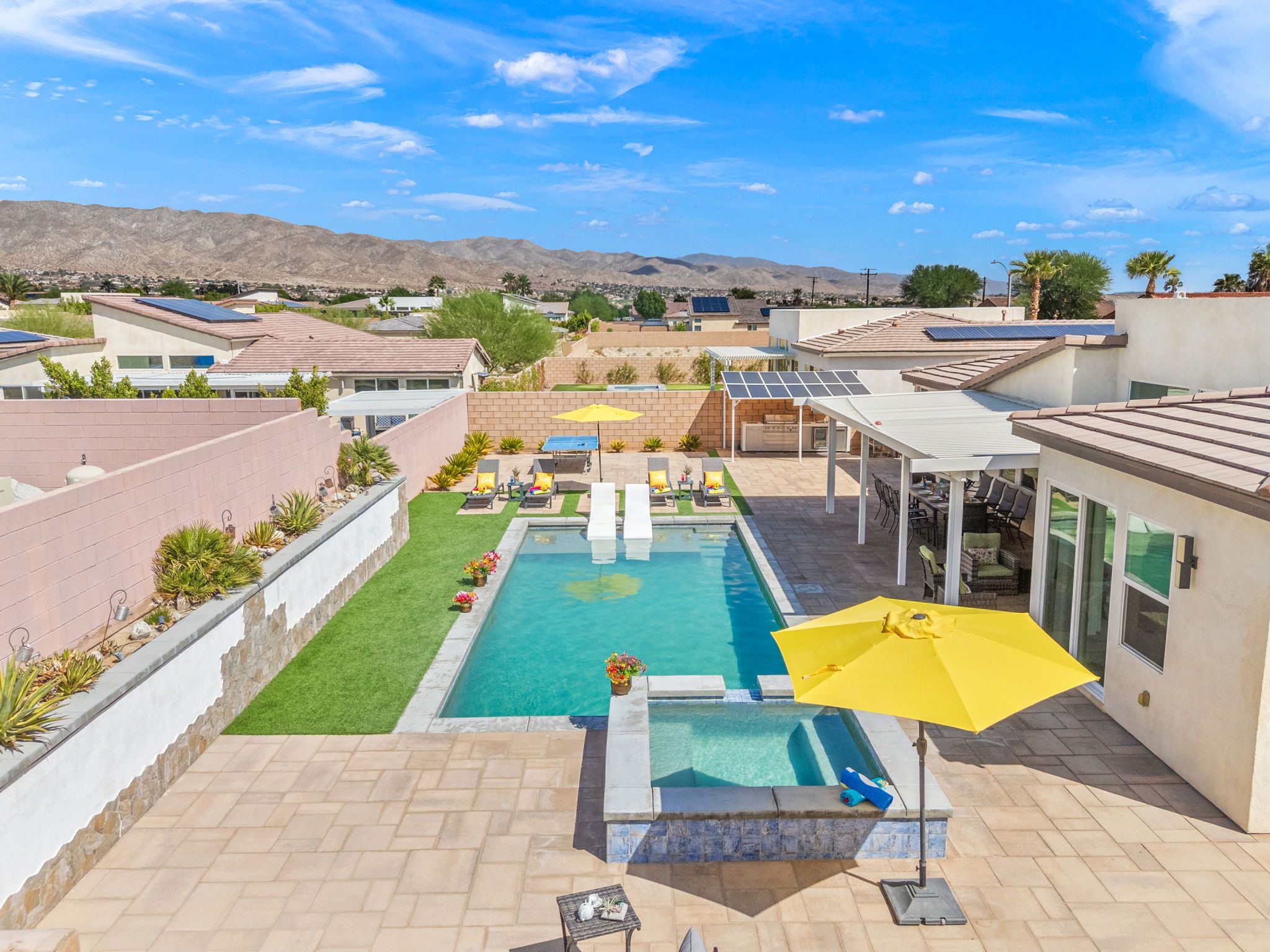 A residential backyard with a swimming pool, patio furniture, and a view of a residential area with houses and mountains.