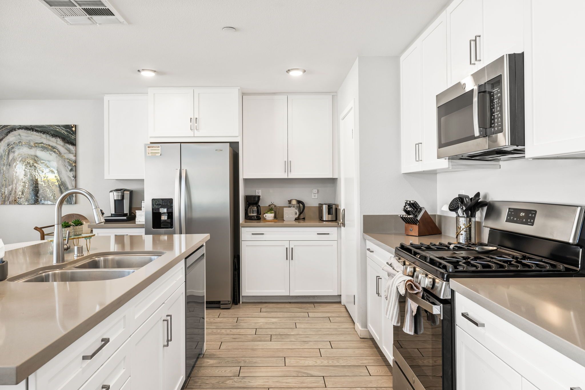 A modern kitchen with white cabinetry, stainless steel appliances, and a wooden floor.