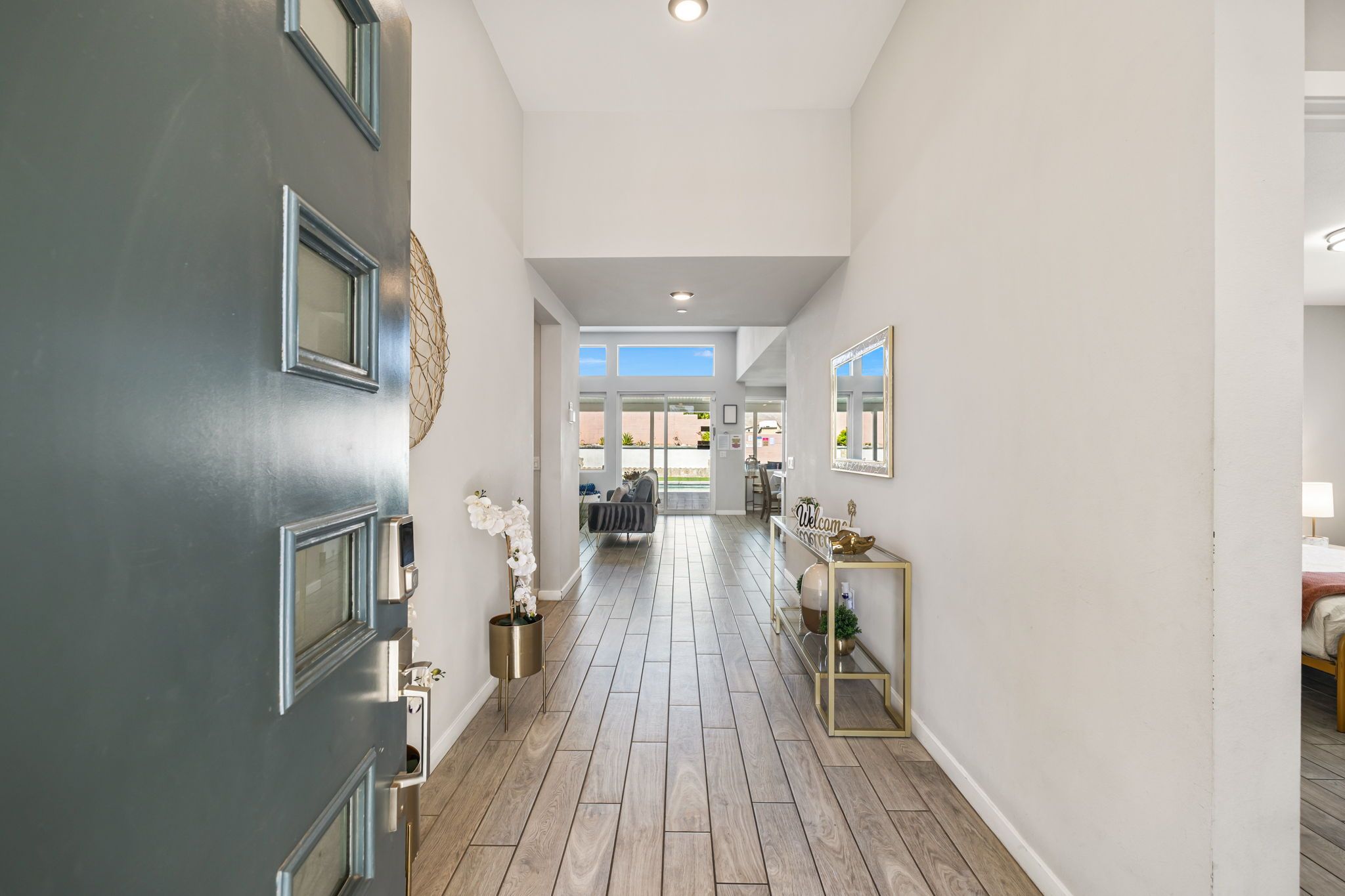 A hallway with a dark door, a mirror, a welcome sign, and a view into a dining area.