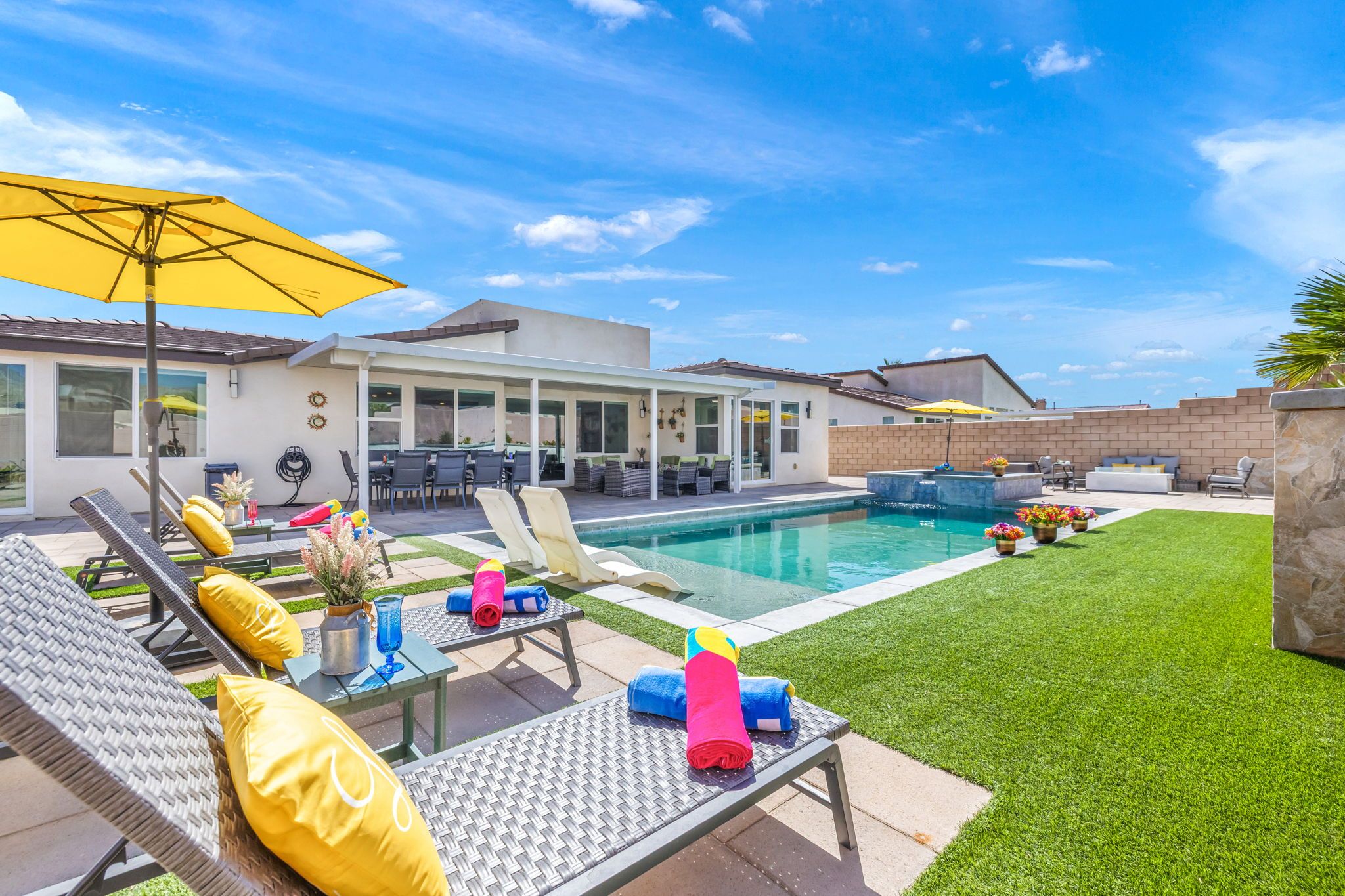 A backyard with a swimming pool, lounge chairs, and a patio area.