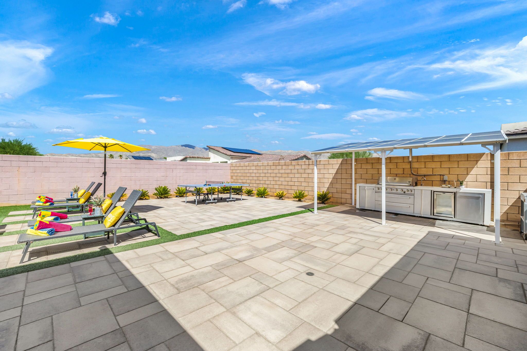 A backyard with a barbecue area, a pool table, and lounge chairs.