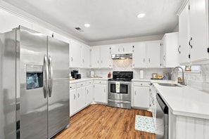 A modern kitchen with white cabinetry, stainless steel appliances, and a herringbone-patterned backsplash. - Spacious 4BR Home in DeRidder (DeRidder)