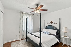 Un llit amb cortines i un ventilador al sostre, roba de llit blanca i un cortinat amb motius florals.