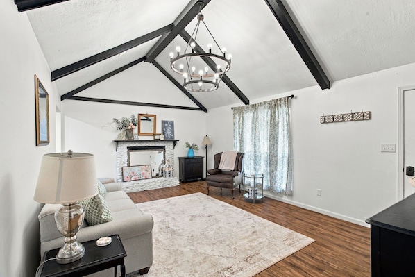 A living room with a fireplace, a chandelier, a sofa, a chair, and a coffee table.