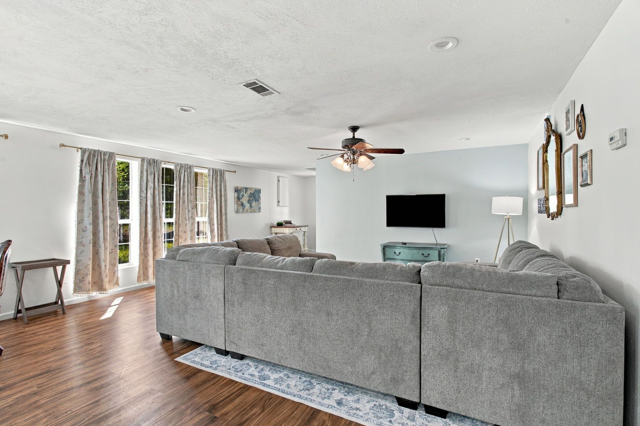 A living room with a sectional sofa, a ceiling fan, a flat-screen TV, and a dining area with a table and chairs.