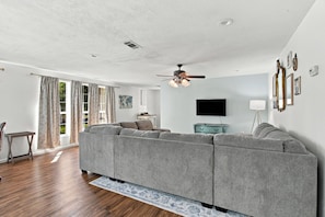 A living room with a sectional sofa, a ceiling fan, a flat-screen TV, and a dining area with a table and chairs. - Spacious 4BR Home in DeRidder (DeRidder)
