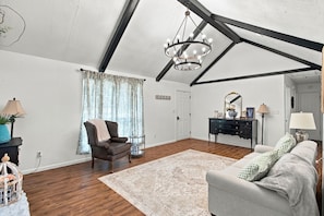 A room with a high ceiling, exposed beams, a chandelier, a brown leather chair, a grey sofa, a wooden floor, and a patterned rug. - Spacious 4BR Home in DeRidder (DeRidder)